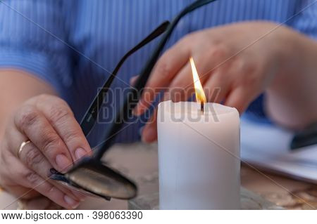 A Lit White Candle, Women's Hands Holding Glasses For Vision. Magician, Sorcerer, Psychologist At Wo