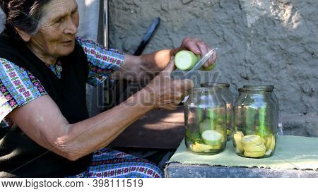 Senior Asian Woman Smiles And Slices Fresh Zucchini With Kitchen Knife. Homemade Canning. Granny Pre