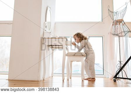 Handsome Little Girl Stands Near Console Table With Mirror And Pulls Drawer Out Of It