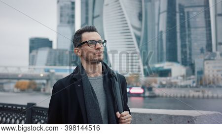 Man In Black Coat And Eyeglasses Walking On Background Of Business Skyscrapers In Moscow, Slow Motio