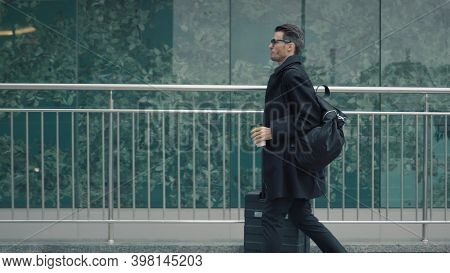 Man In Black Coat Walking On Background Of Glass Buildings, With Suitcase And Bag Slow Motion. Busin