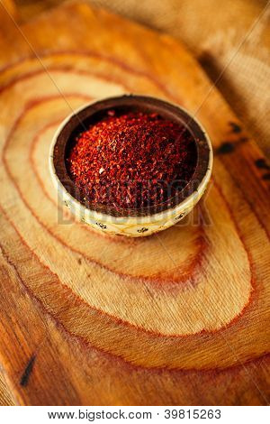 Red hot chilli pepř vločky v misce na dřevěném prkénku pozadí, mělké dof