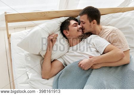 Happy Gay Couple Lying On Bed At Home Top View