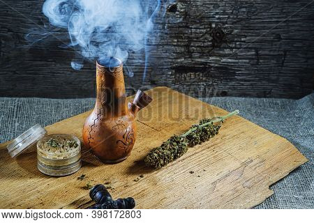 Old Brown Steamung Bong And Open Cannabis Grinder With Chopped Marijuana Weed And Medical Cannabis I