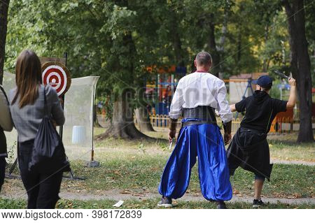 The Attraction Of Throwing Knives In A Park. Boy Throws Knives Into A Target