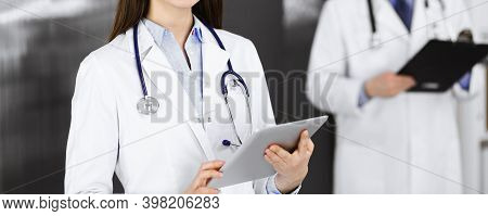 Unknown Woman Doctor Iusing Tablet Computer In Her Hands, While Standing In Clinic. Medicine Concept