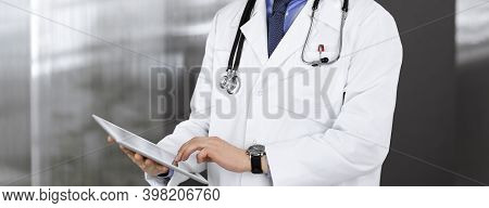 Unknown Male Doctor Iusing Tablet Computer In His Hands, While Standing In Clinic. Medicine Concept 