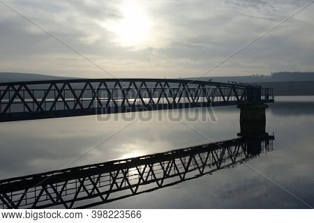 Birds Settle On A Metal Jetty With Calm Water And Evening Sunlight Reflected Behind. Hazy Atmosphere