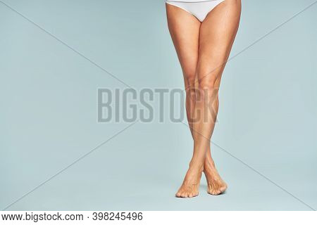 Perfect Hair Removal. Cropped Shot Of A Woman With Perfectly Shaven Legs Standing Over Blue Backgrou