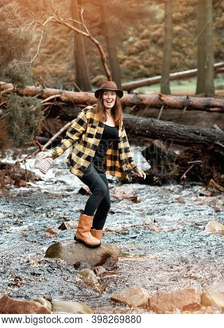 Woman In Yellow Shirt And Hat Walking Along The River In The Autumn Forest