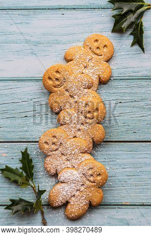 Gingerbread Cookies Or Gingerman Arranged On A Blue Wooden Table With Holly, Traditional Christmas P
