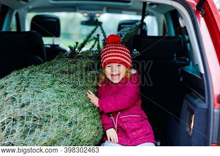 Adorable Little Toddler Girl With Christmas Tree Inside Of Family Car. Happy Healthy Baby Child In W