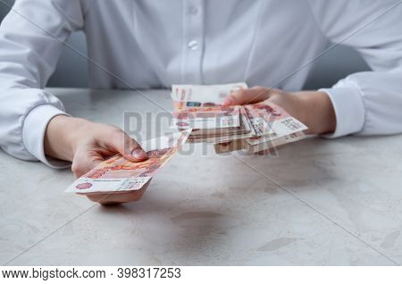 A Girl In A White Shirt At A Table Holds Money In Her Hands, The Concept Of Big Money
