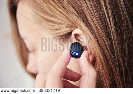 Woman Listening Music Through Wireless Earphones. Caucasian Woman Using Bluetooth Headhones In The E