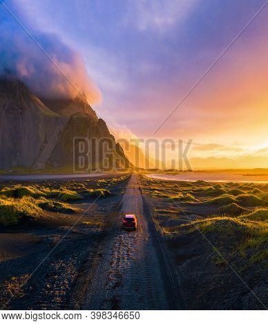 Gravel Road At A Golden Sunset With Vestrahorn Mountain In The Background And A Car Driving The Road