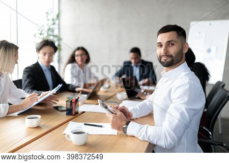 Arab Businessman At Business Conference, Holding Digital Tablet Sitting At Desk Meeting With Mixed C