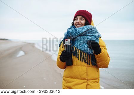 Young Woman Pours Hot Tea From A Thermos Into A Cup And Drinks On The Seaside. Female Tourist Is Hav