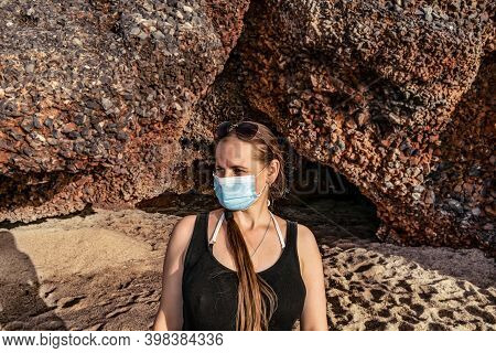 Real Young Adult Girl In A Medical Mask And Sunglasses On Her Head Against The Backdrop Of Cave On K