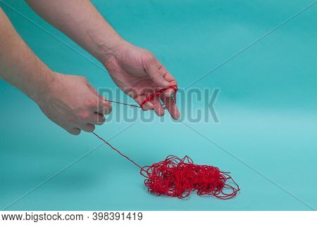 A Man Rolls The Thread Into A Tangle. The Man Begins To Reel The Red Thread On His Fingers From The 