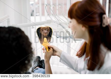 Back View Of Beautiful African Woman Patient And Caucasian Female Dentist, Checking Smile After Curi