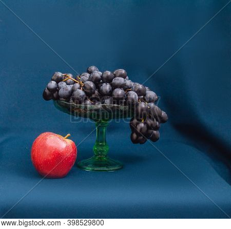 Washed Bunches Of Ripe Blue Grapes And Red Apples Covered With Water Drops In An Old Glass Fruit Bow