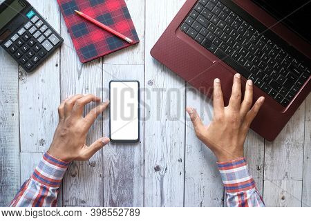 Top View Of Man Hand Using Smart Phone And Typing On Laptop