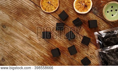 Coals For Hookah On Wooden Background With Dry Oranges, Tobacco And Bowl. Place For Text