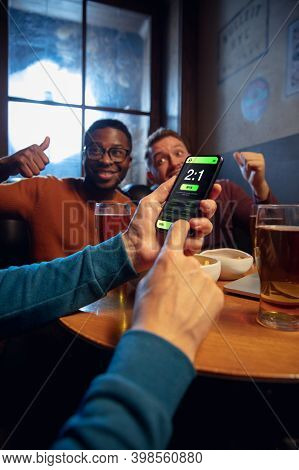 Tensioned. Excited Fans In Bar With Beer And Mobile App For Betting, Score On Their Devices. Screen 