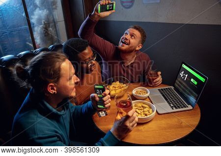 Analyzing. Excited Fans In Bar With Beer And Mobile App For Betting, Score On Their Devices. Screen 