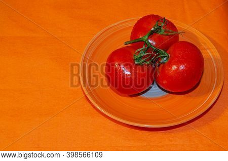 Round Red Tomatoes On A Branch With A Colored Background And Water Drops