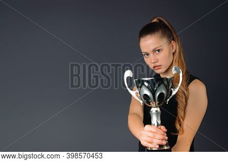 Successful, Young Businesswoman With Her Trophy On A Gray Background With Empty Side Space.