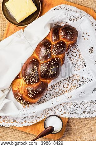 Fresh Homemade Challah With Sesame Seeds On A White Lace Napkin. Salt And Butter On The Table. Top V