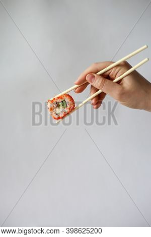 Hand Of A Young Woman Holding Sushi Sticks And A Philadelphia Roll