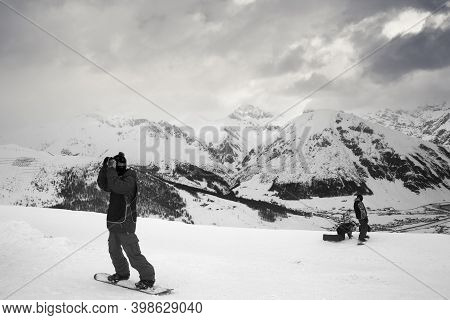 Group Of Snowboarders Starts On Off-piste Descent. High Snowy Mountains And Cloudy Storm Sky At Wint