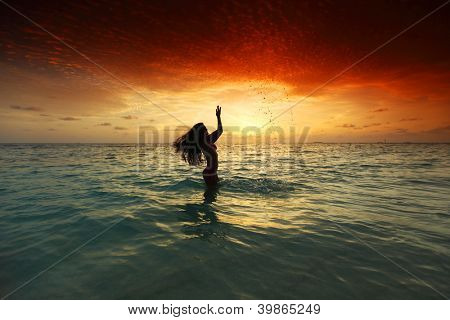 Vrolijke vrij jonge vrouw splashin in zee op zonsondergang