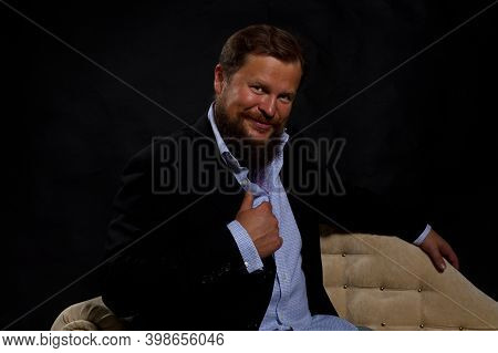 Smilingl Solid Bearded Man Dressed In Suit Sitting On Sofa Studio Portrait