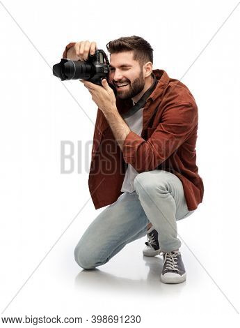 photography, profession and people and concept - happy smiling man or photographer with digital camera staying on one knee and taking picture over white background