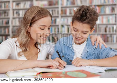 Close Up Of A Cheerful Beautiful Wman Helping Her Son With School Assignment At The Library