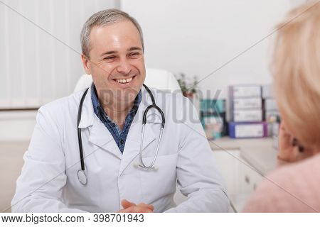 Cheerful Mature Male Doctor Laughing, Talking To His Female Patient. Experienced Male Doctor Smiling