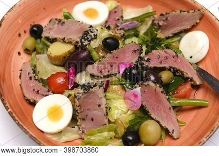 Salad With Meat Slices, Potatoes, Olives And Boiled Egg On A Brown Plate