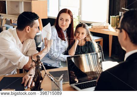 Frustrated Father In Suit Sits On Couch Next To Young Wife And Daughter. A Man Sits In A Suit And Lo
