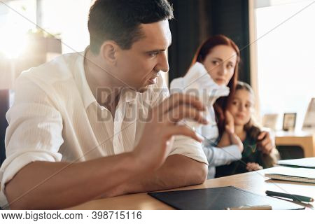 Frustrated Father In Suit Sits On Couch Next To Young Wife And Daughter. A Man Sits In A Suit And Lo