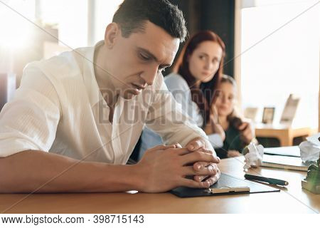 Frustrated Father In Suit Sits On Couch Next To Young Wife And Daughter. A Man Sits In A Suit And Lo