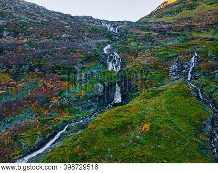 Long Narrow Waterfall Cutting Through The Terrain On A Steep Green Mountain Slope. 4k Aerial Footage