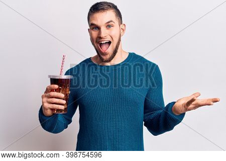 Young handsome man dirnking cola refreshment beverage celebrating achievement with happy smile and winner expression with raised hand 