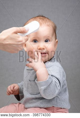 Pediatrician or nurse checks baby girl's body temperature using infrared forehead thermometer (thermometer gun) for virus symptoms