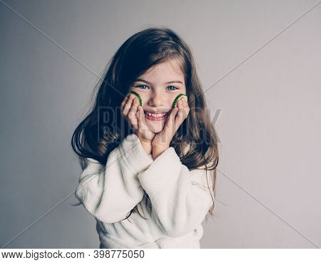 Funny Little Girl With Cucumbers On Her Face , Beauty And Health Concept, Closeup Portrait.