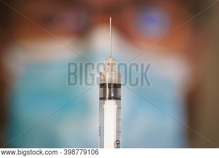 Close-up Of Hypodermic Syringe With Blurred Doctor On The Background.