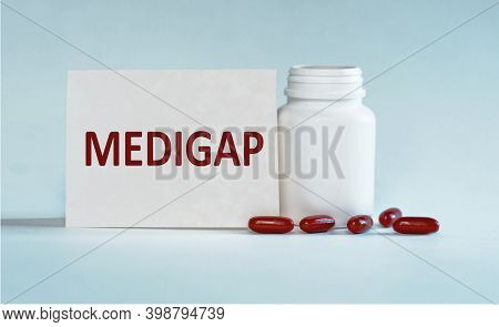 On A Light Blue Background A Card With The Text Medigap Near The White Bottle Pills