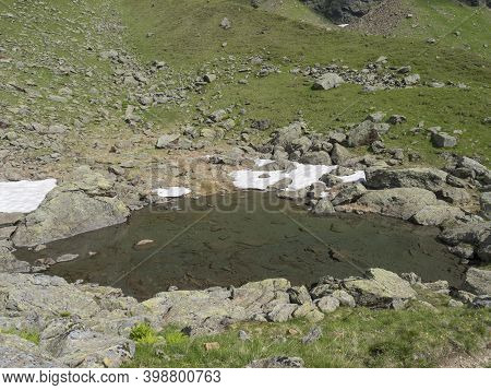 Small Pond From Melting Snow With Rock And Stones At Alpine Meadow. Tyrol, Stubai Alps, Austria